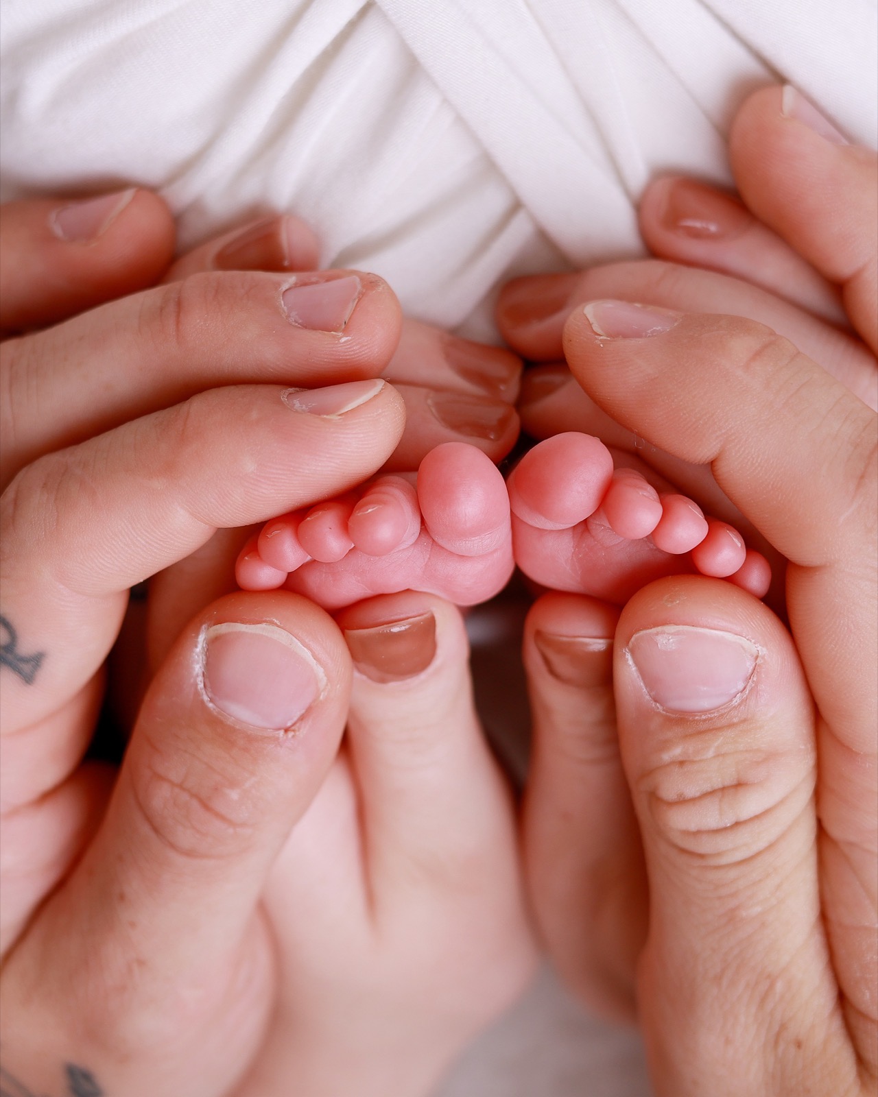 Close-up of two parents' hands cradling their newborn's tiny feet together
