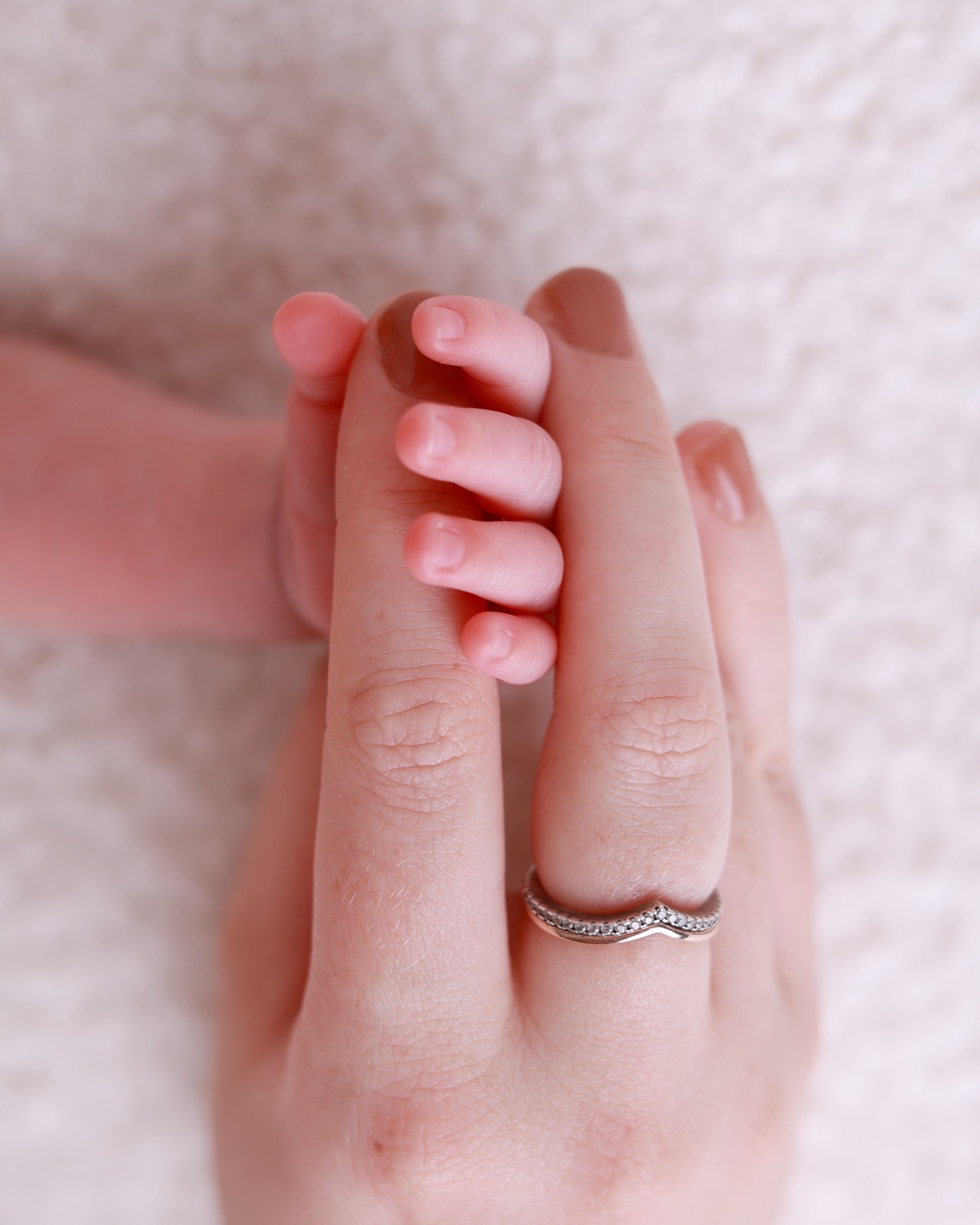 Extreme close-up of a newborn's fingers curled around a parent's fingers, a diamond ring visible