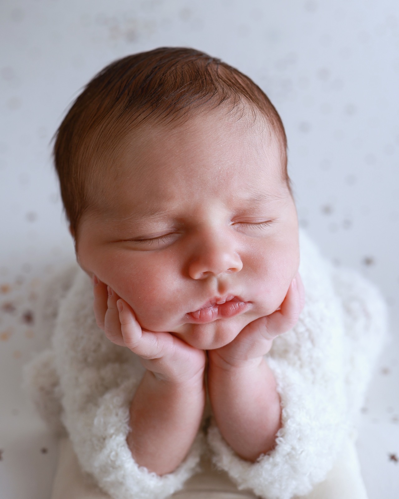 Close-up of a sleeping newborn resting her chin on her hands, speckled backdrop