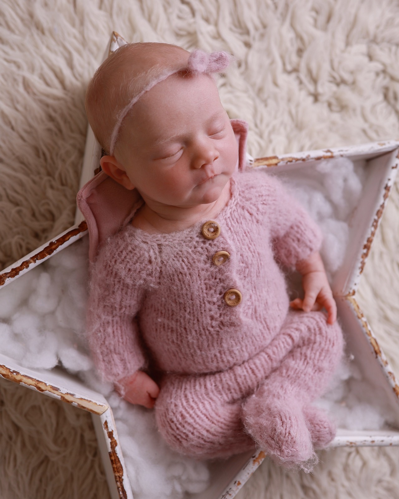 Sleeping newborn girl in a dusty pink knitted romper with wooden buttons, tiny felt bow headband, wooden star prop