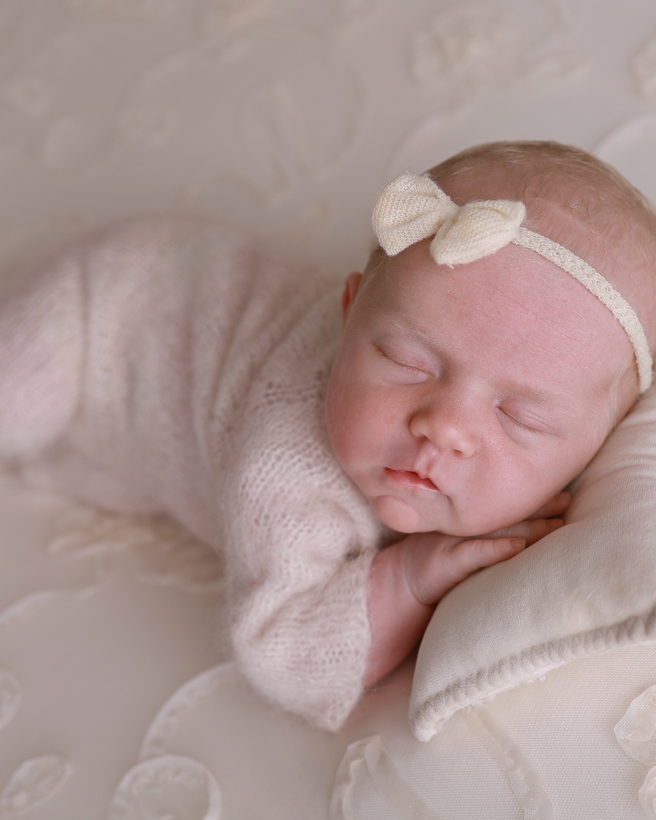 Close-up profile of a sleeping newborn girl, cream tulle bow headband, cream knitted outfit