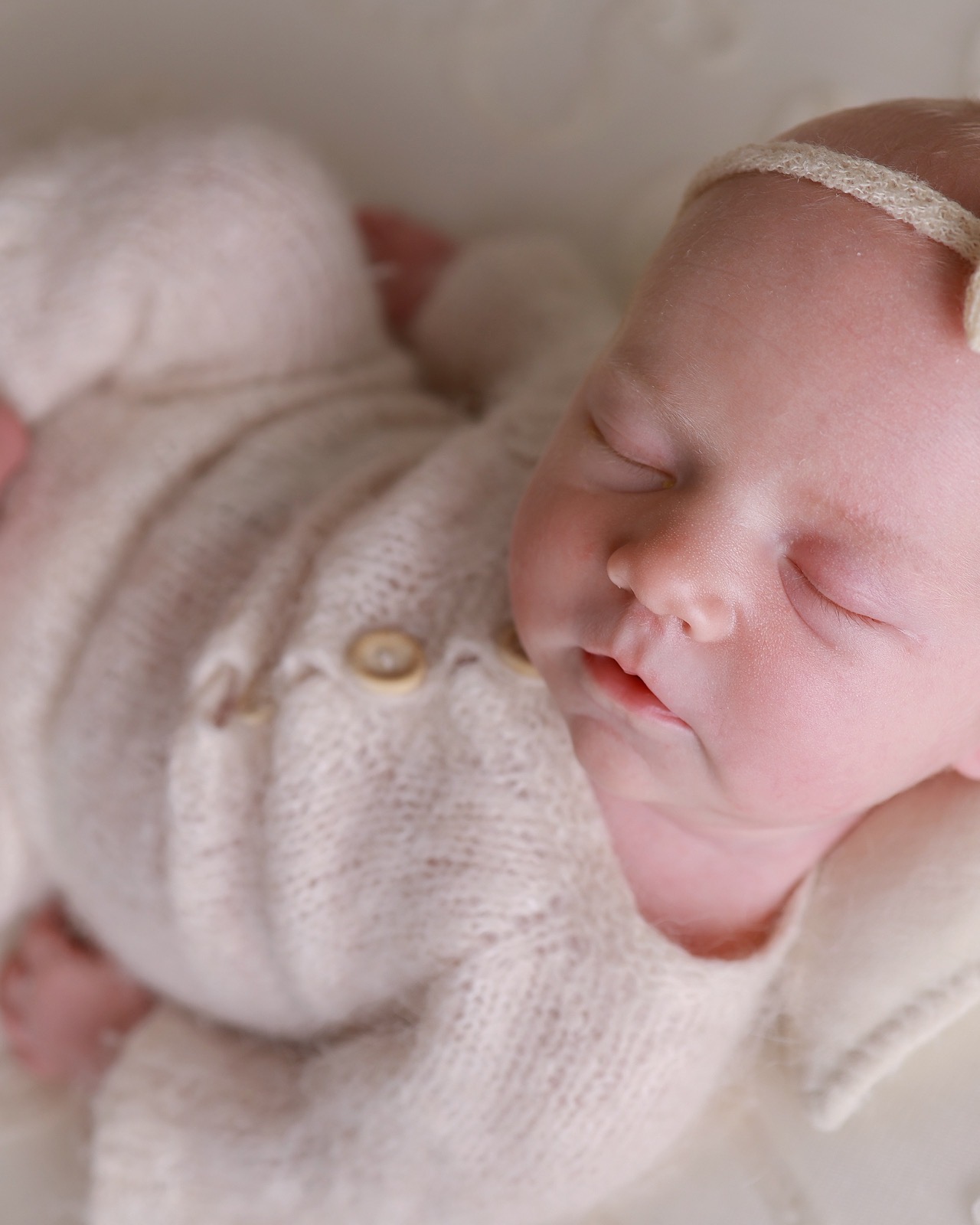 Close-up of a sleeping newborn nuzzled into a cream knitted outfit with wooden buttons