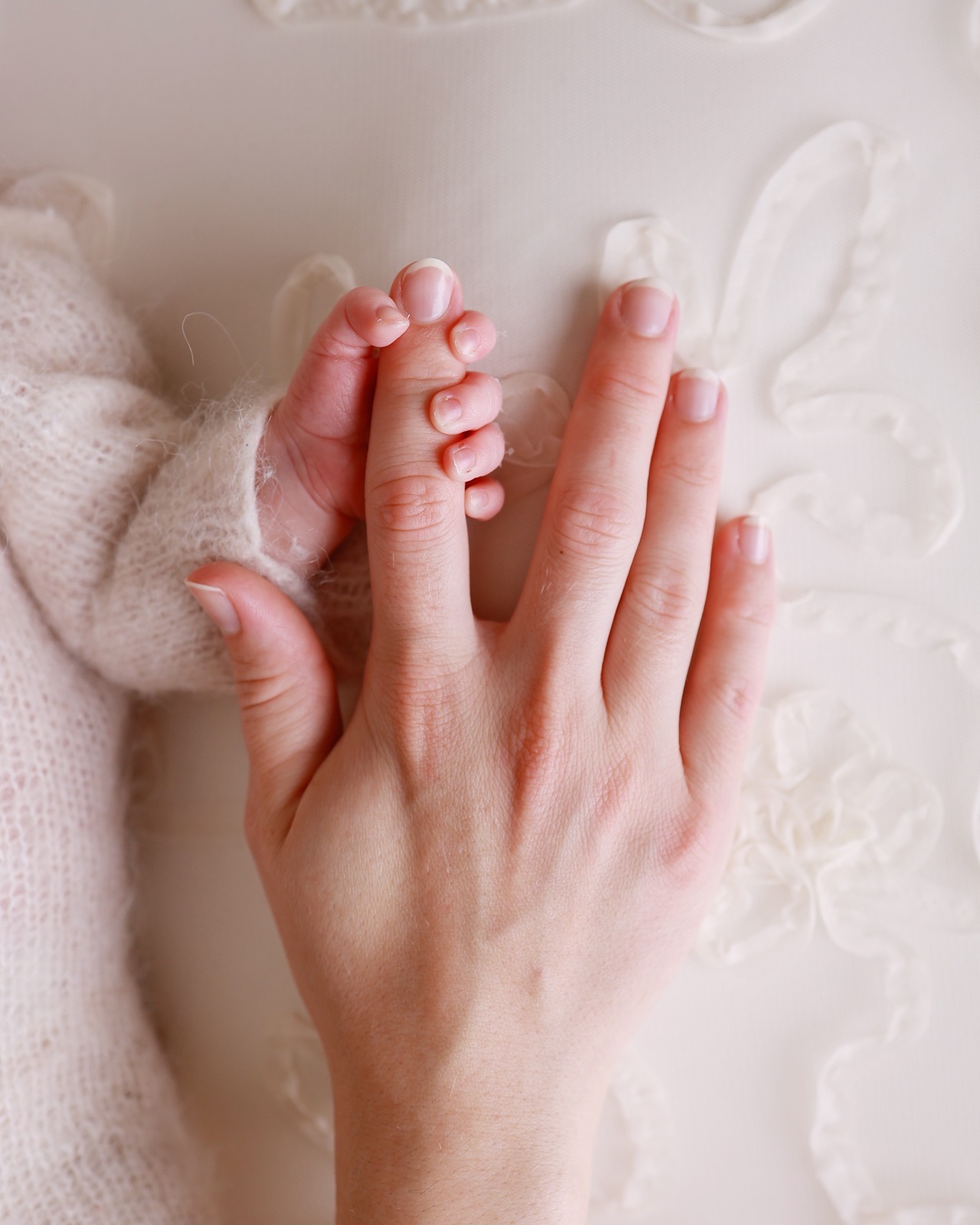 Extreme close-up of a newborn's hand gripping a parent's fingers, resting on embroidered fabric