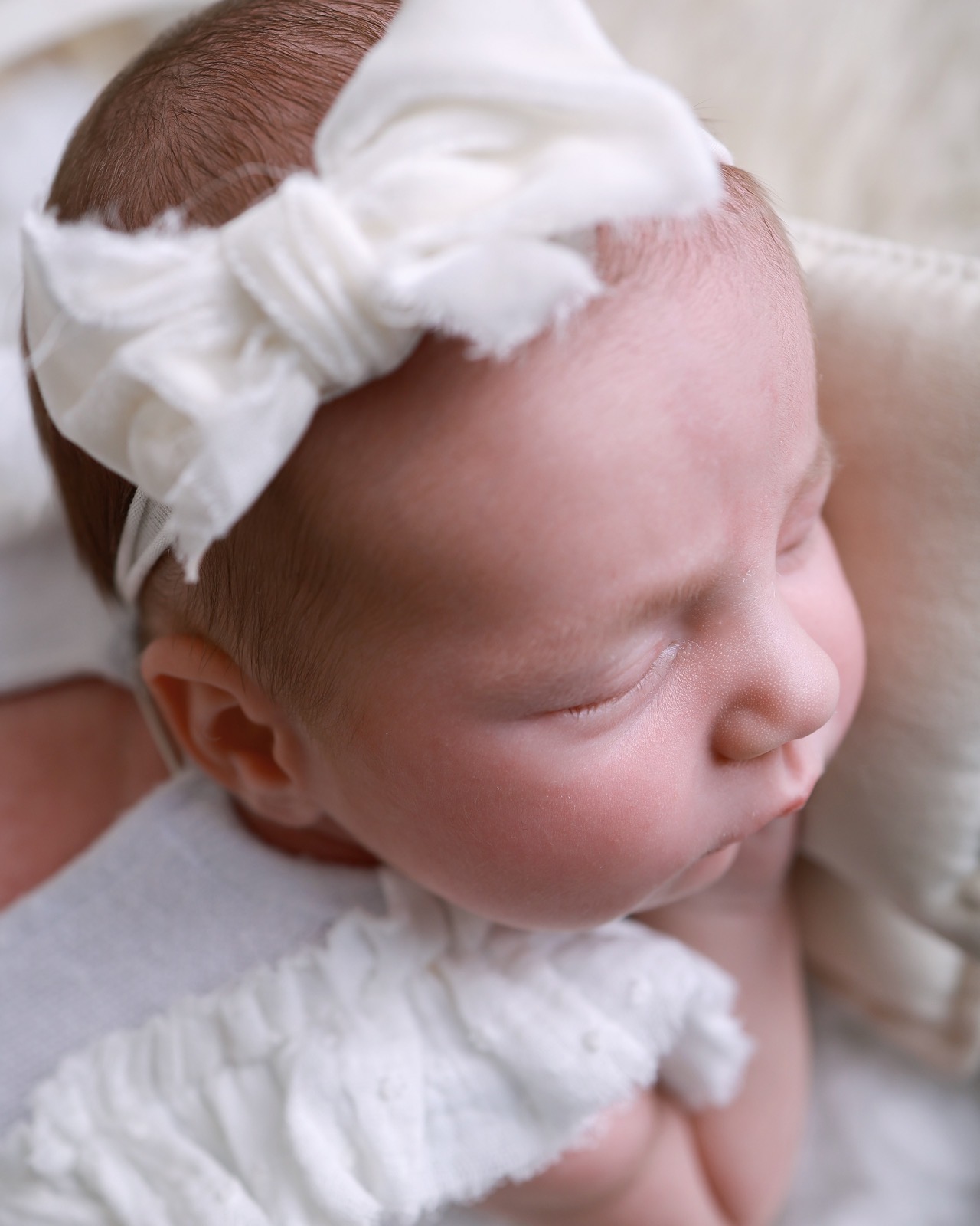 Close-up profile of a sleeping newborn, cream bow headband, resting on a cream cushion