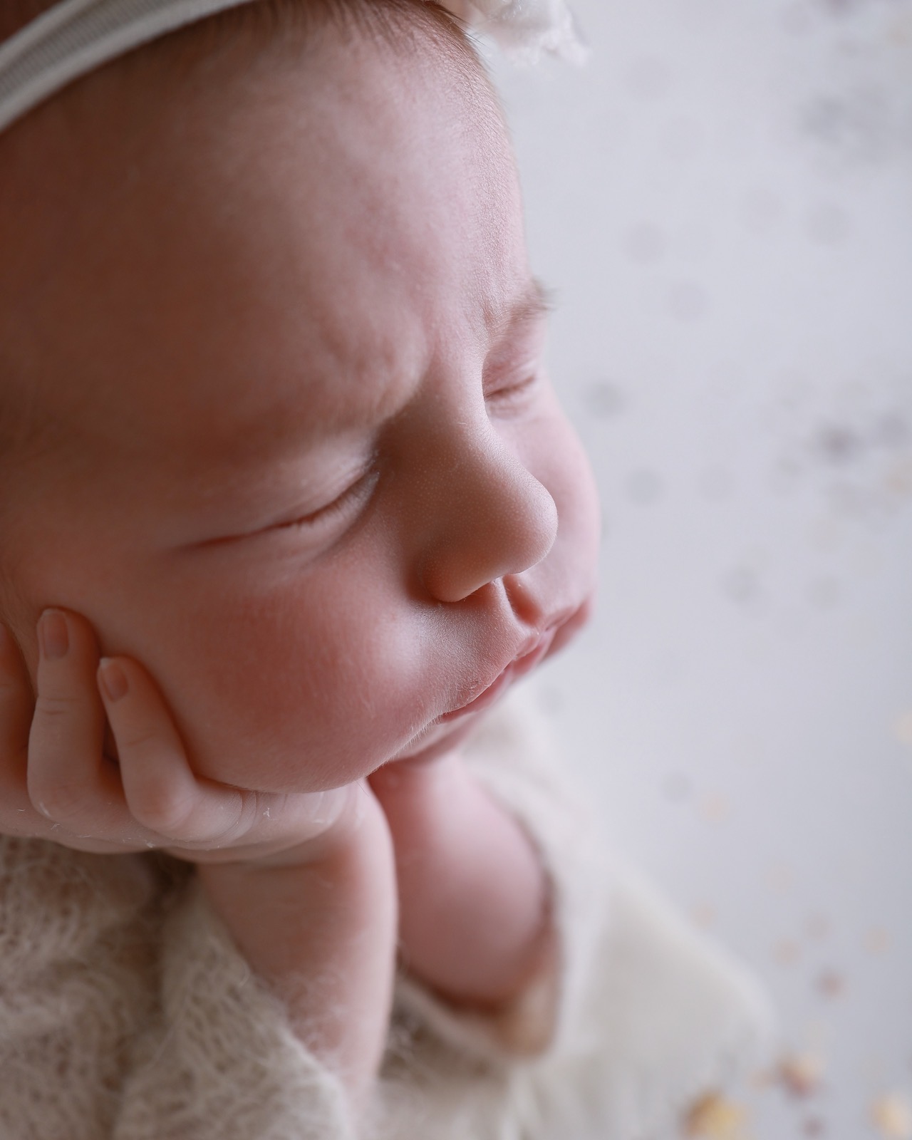 Extreme close-up of a sleeping newborn's face, hand resting on her cheek, star-speckled backdrop