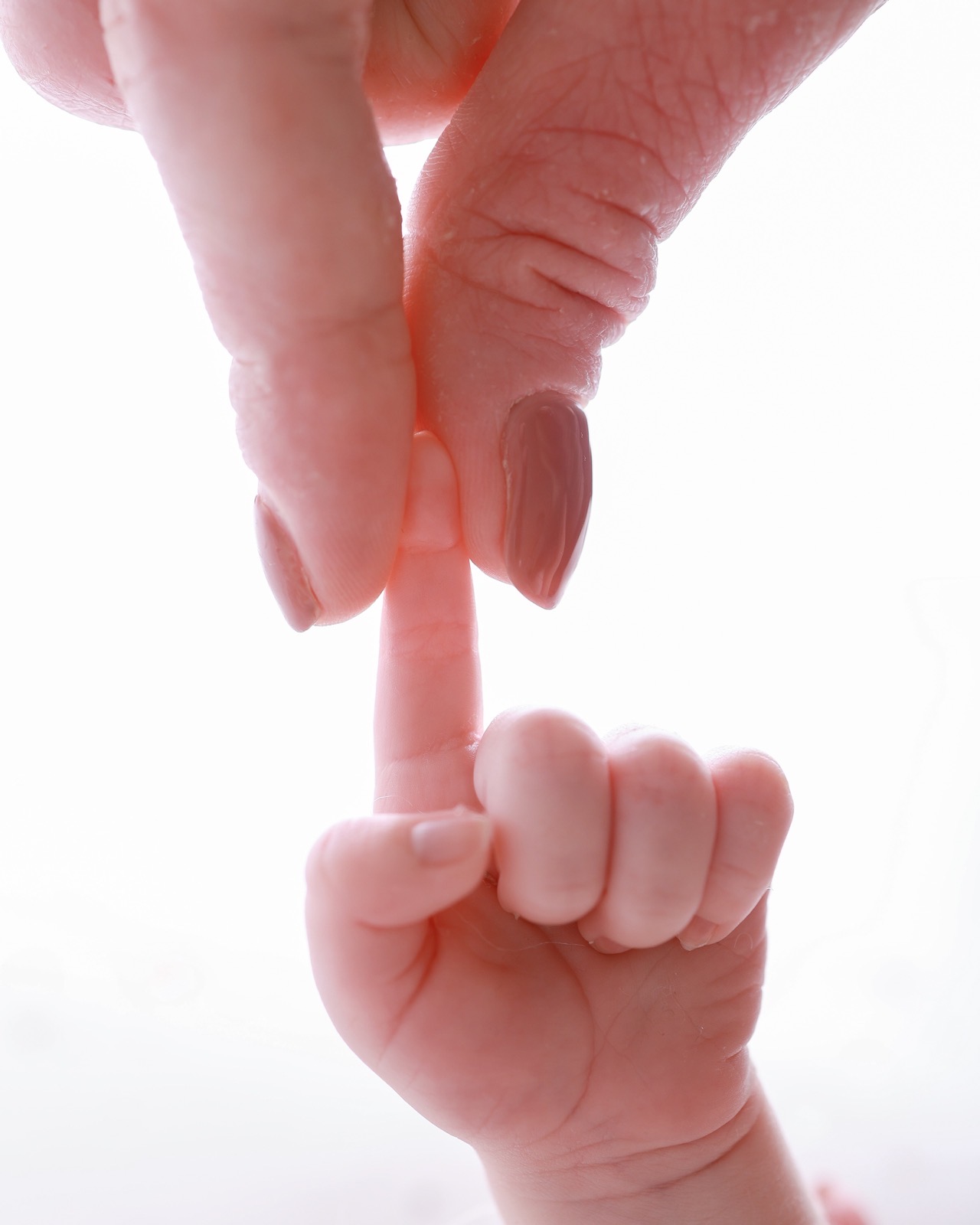 Extreme close-up of a parent's finger held in a newborn's fist, backlit
