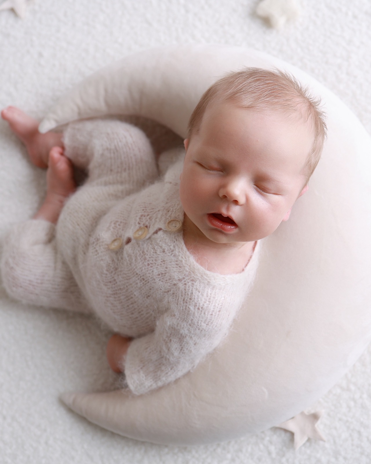 Sleeping newborn boy in an oatmeal knitted outfit lying in a crescent-moon cushion prop