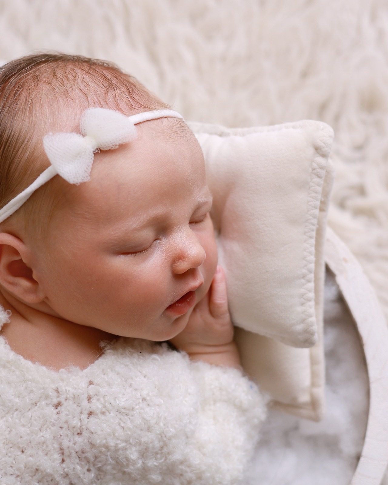 Close-up profile of a sleeping newborn, small white bow headband, hand near her cheek