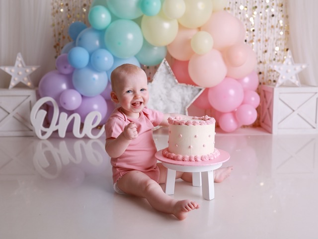 Baby laughing upside down over a first birthday cake, from a cake smash session