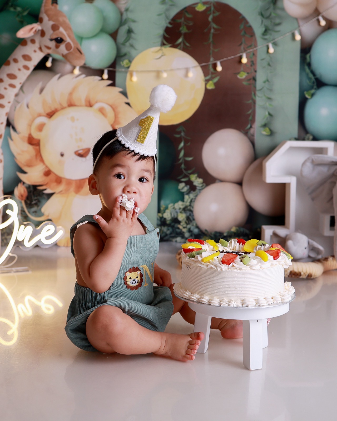 Toddler boy eating cake with his fingers, safari-themed backdrop with lion and giraffe illustrations