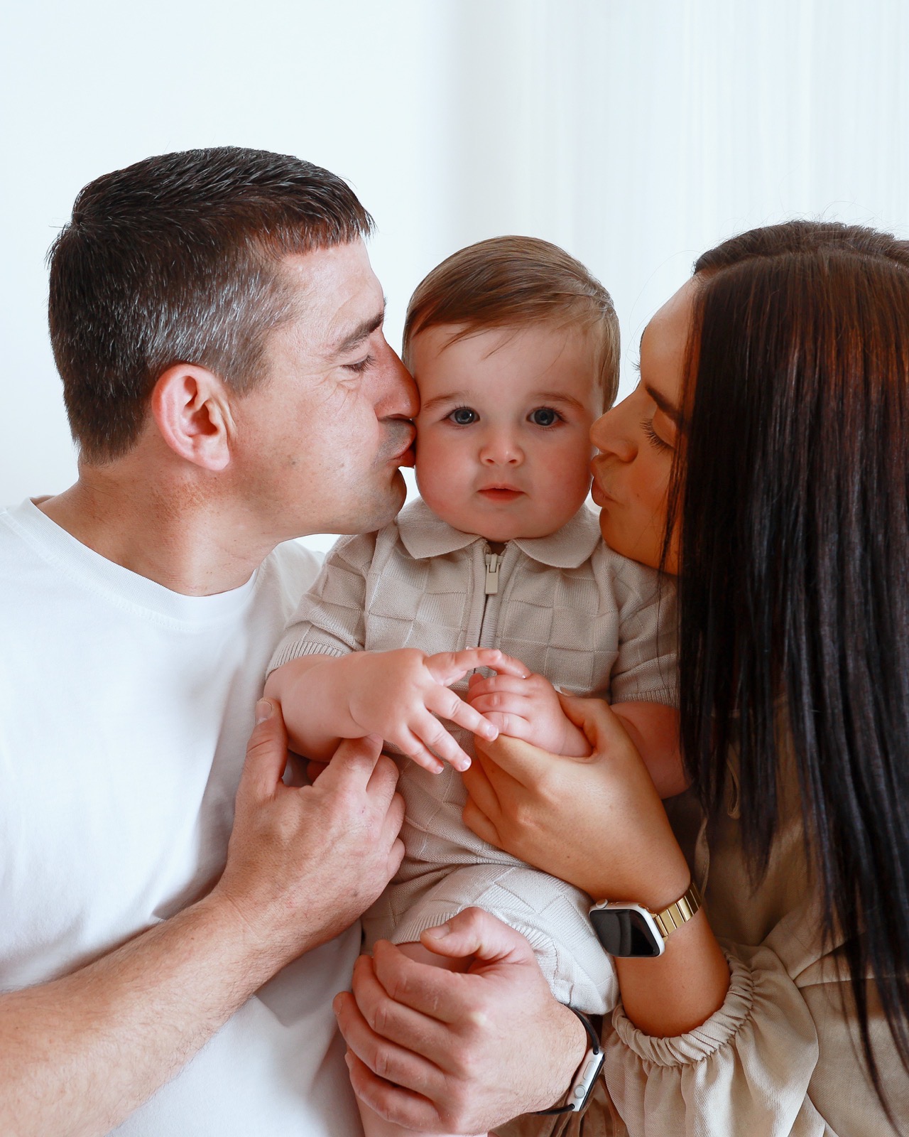 Dad and mum each kissing their toddler son on the cheek