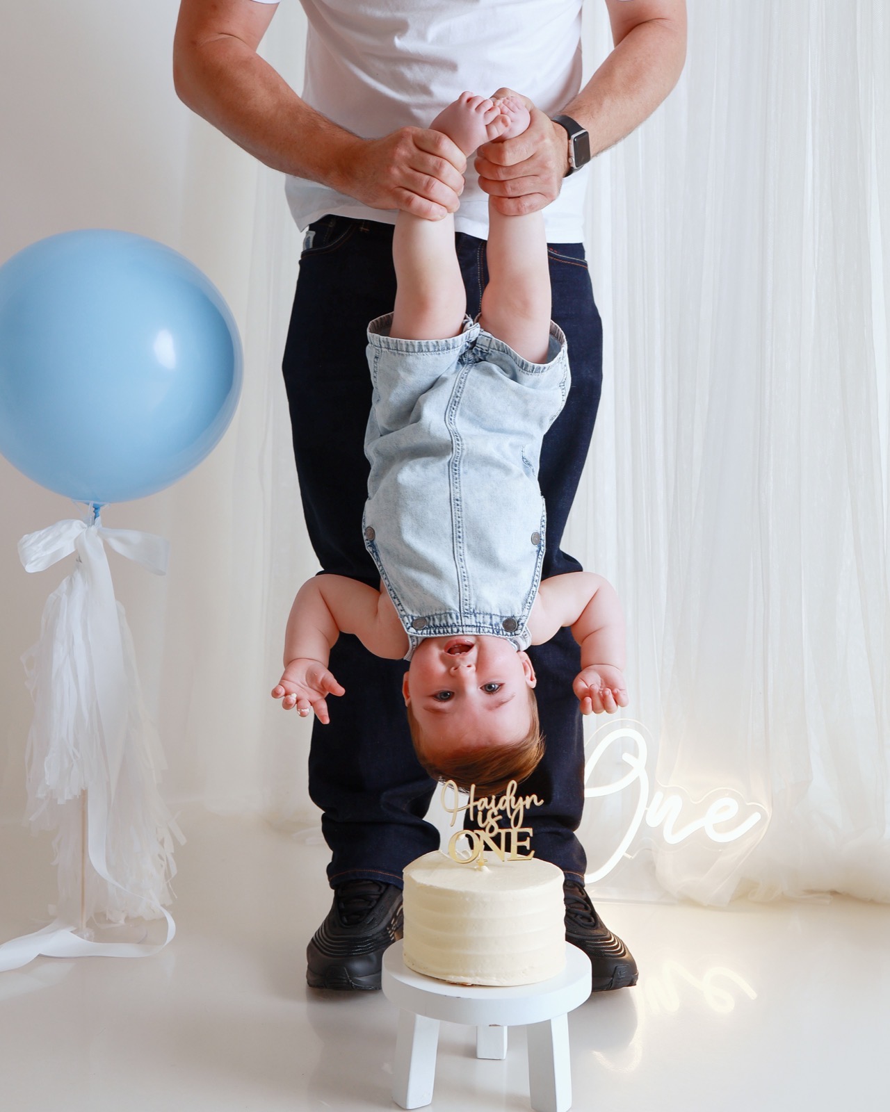 Dad holding a toddler boy upside down by the ankles in front of a birthday cake, playful moment