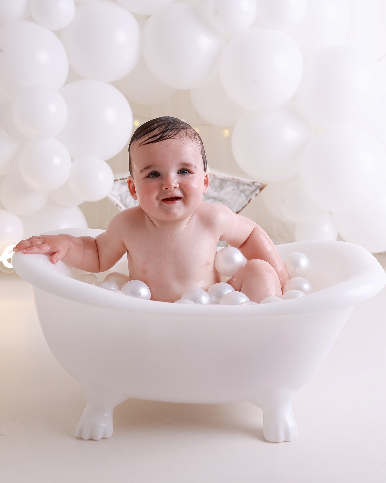 Toddler boy resting his arm on the edge of a white bath tub filled with pearl-white bath balls