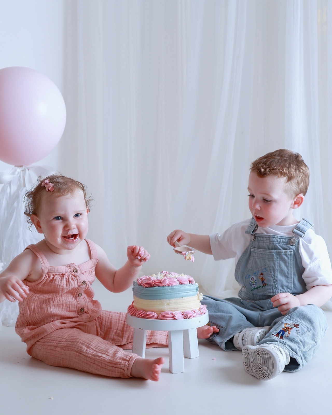 Twin siblings with cake on their faces, brother about to feed his sister another spoonful