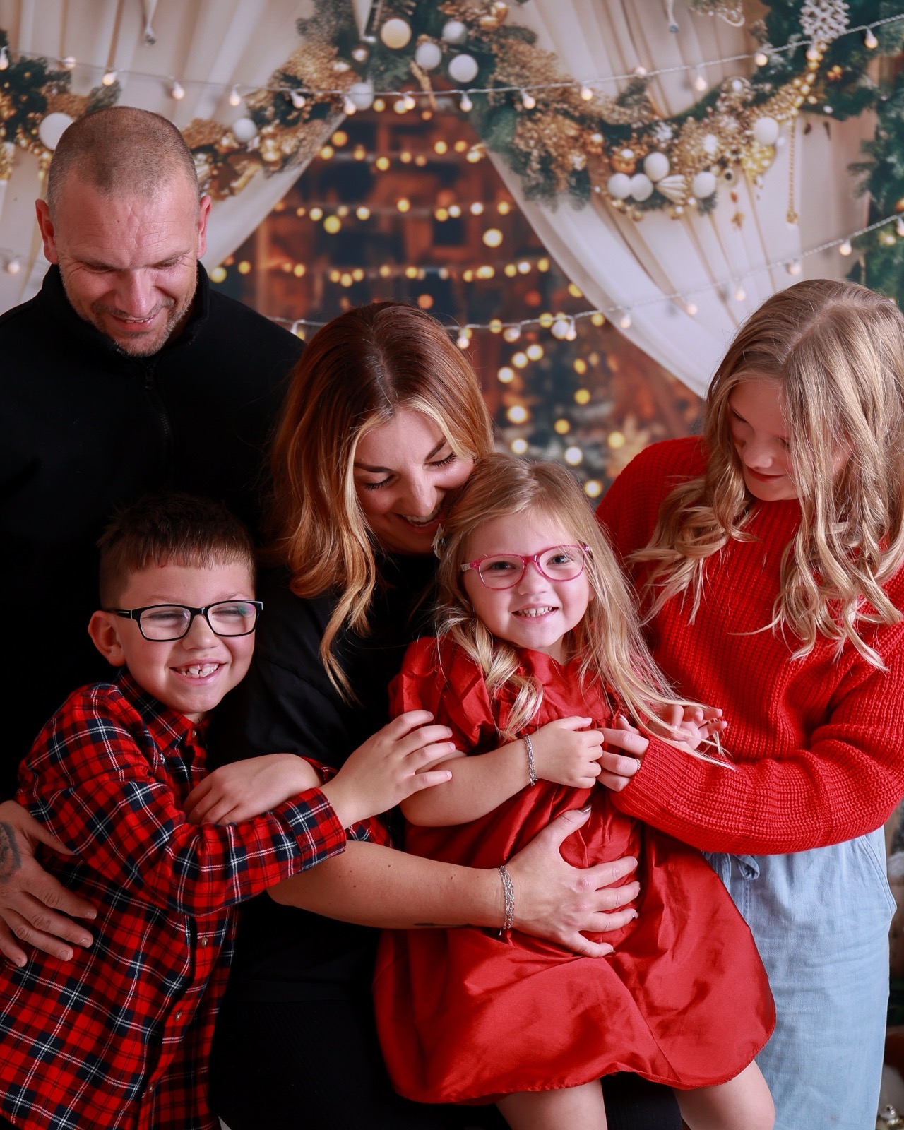 Family embracing together, dad and youngest daughter in red plaid, mum in red, older daughter in a red jumper