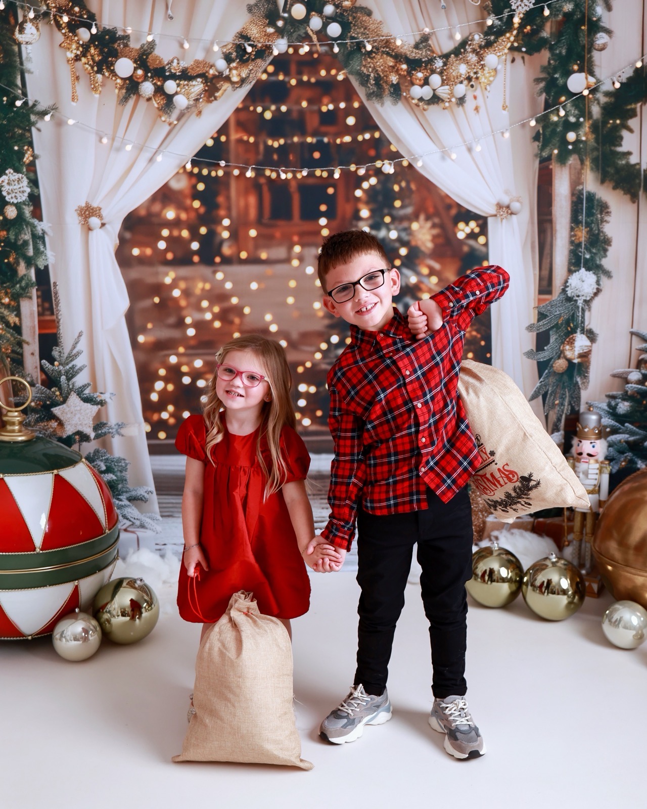 Brother and sister holding hands, both dressed in red, each holding a hessian gift sack