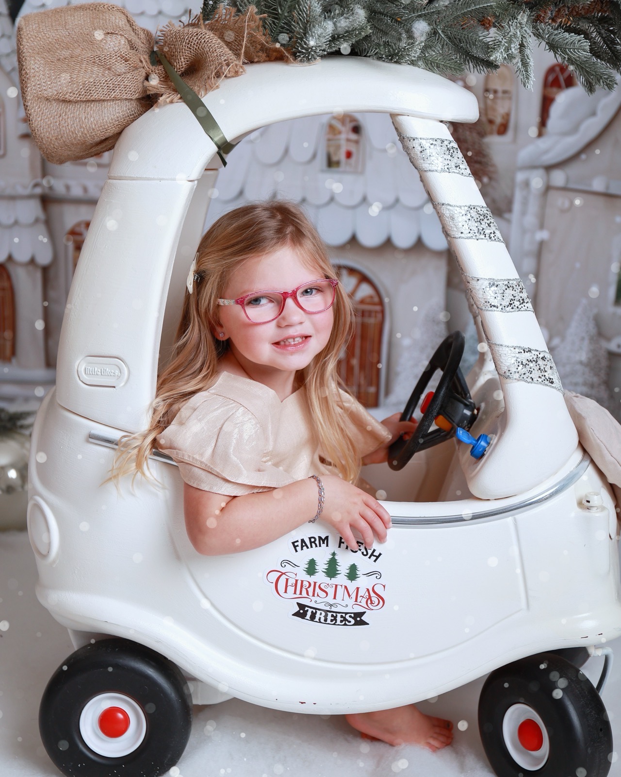 Girl in a gold dress sitting in a toy car under a snowy pine branch, 'Farm Fresh Christmas Trees' sticker