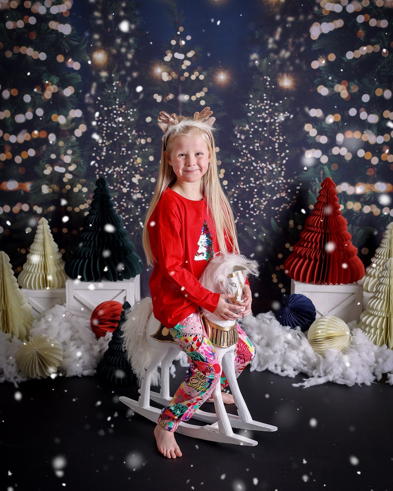 Girl in a red sequin-tree top riding a white fluffy rocking horse, starry night backdrop