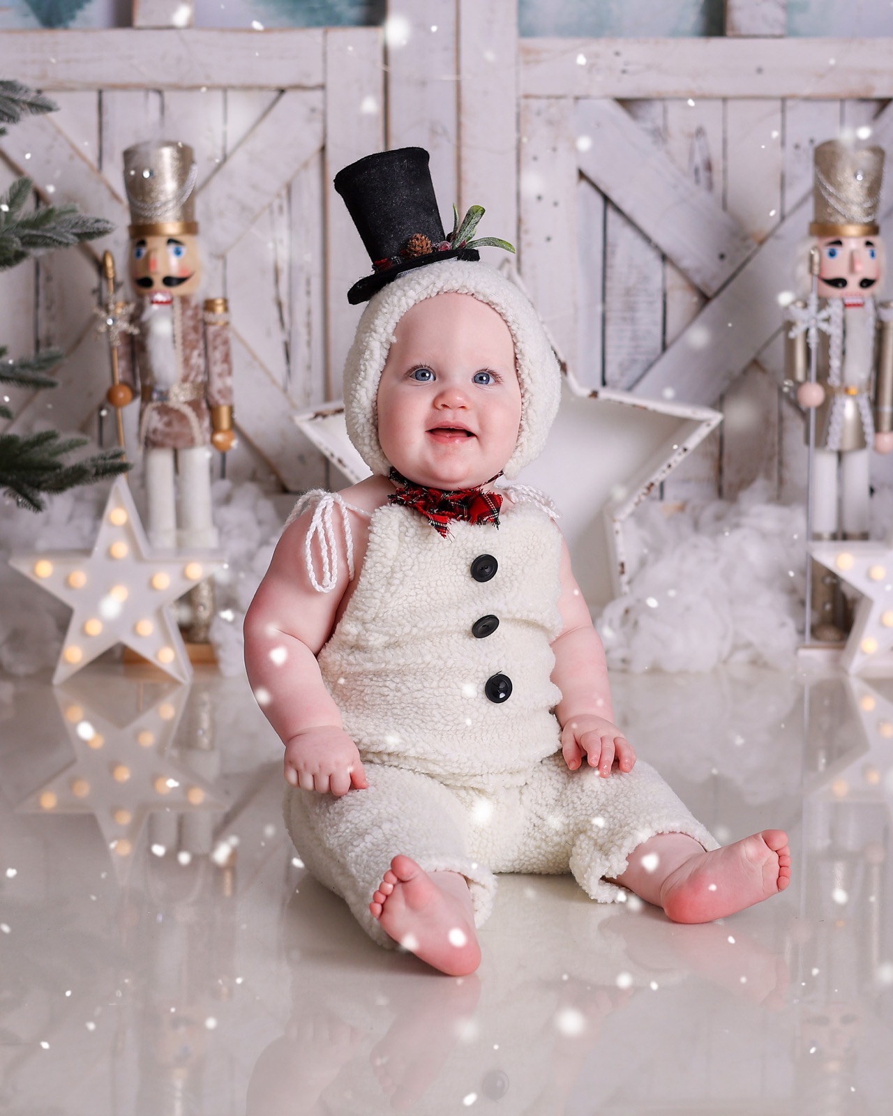Baby in a snowman costume with a black top hat and tartan bow tie, seated between nutcracker figures