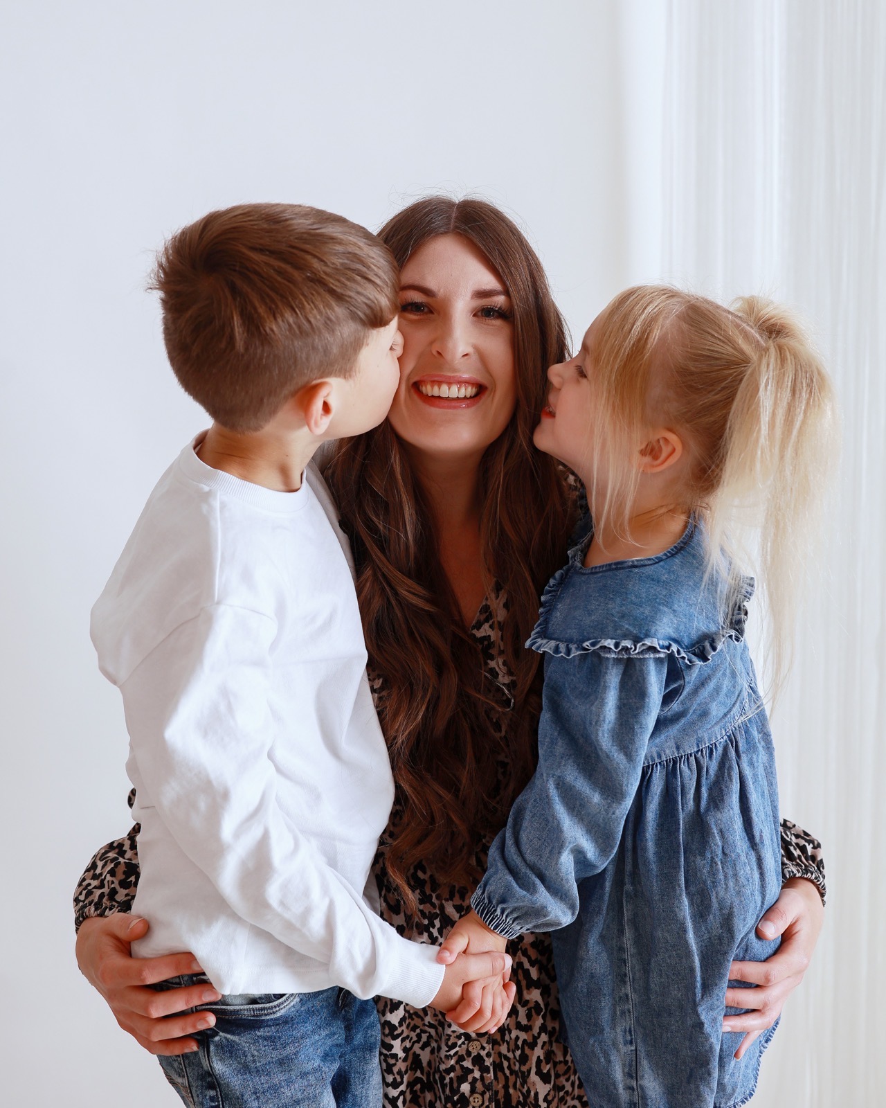Mum in a leopard-print dress receiving a kiss on each cheek from her son and daughter