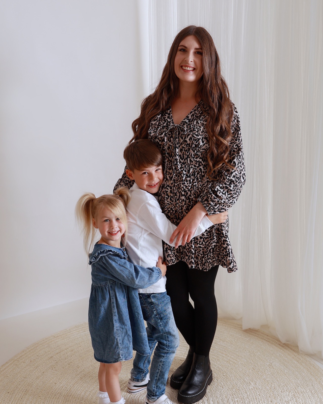 Mum in a leopard-print dress standing as her son and daughter hug her from either side