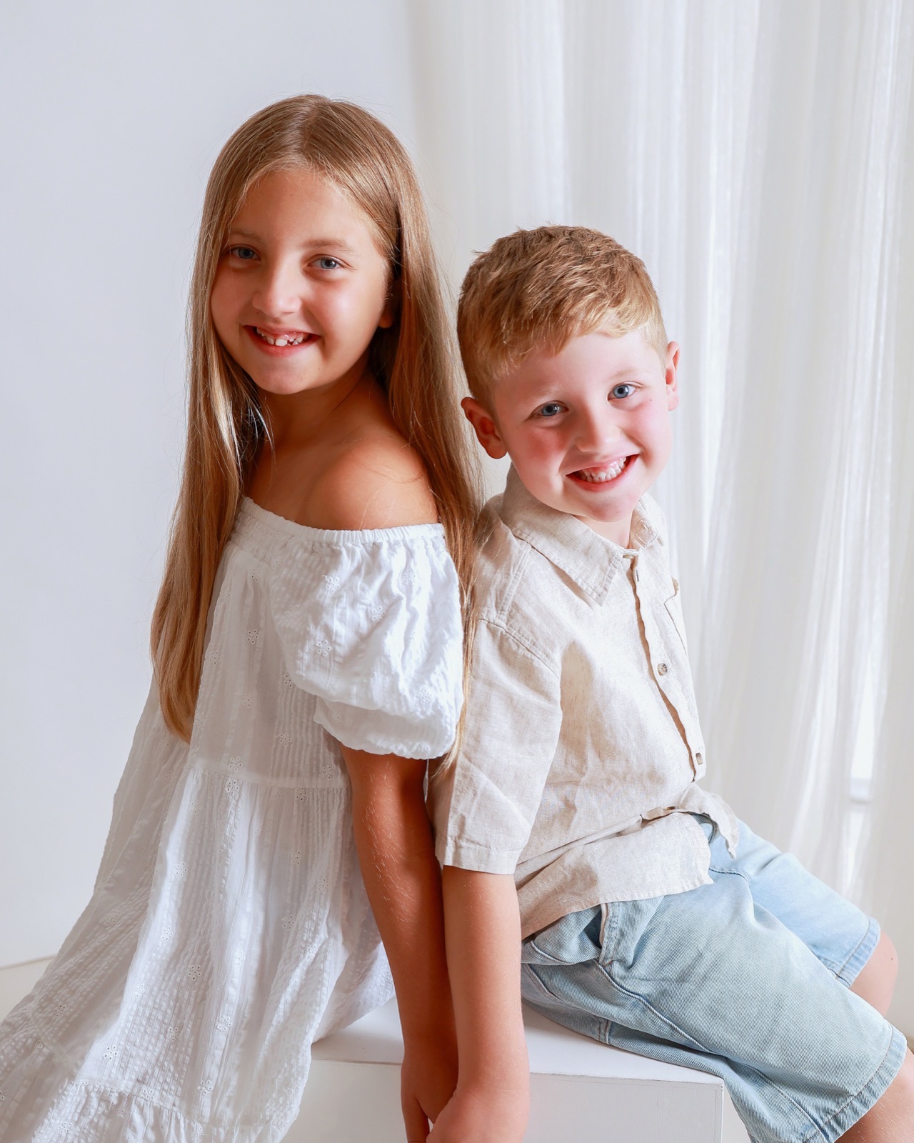Older sister and younger brother facing forward together, smiling