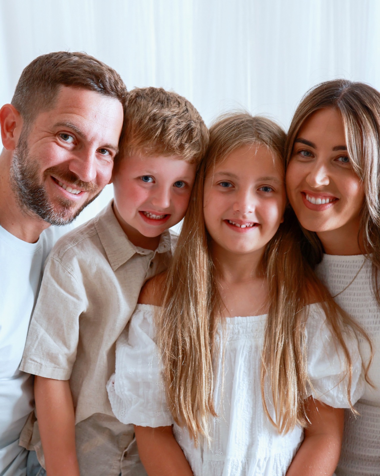Close-up portrait of a family of four, heads gathered together, all smiling