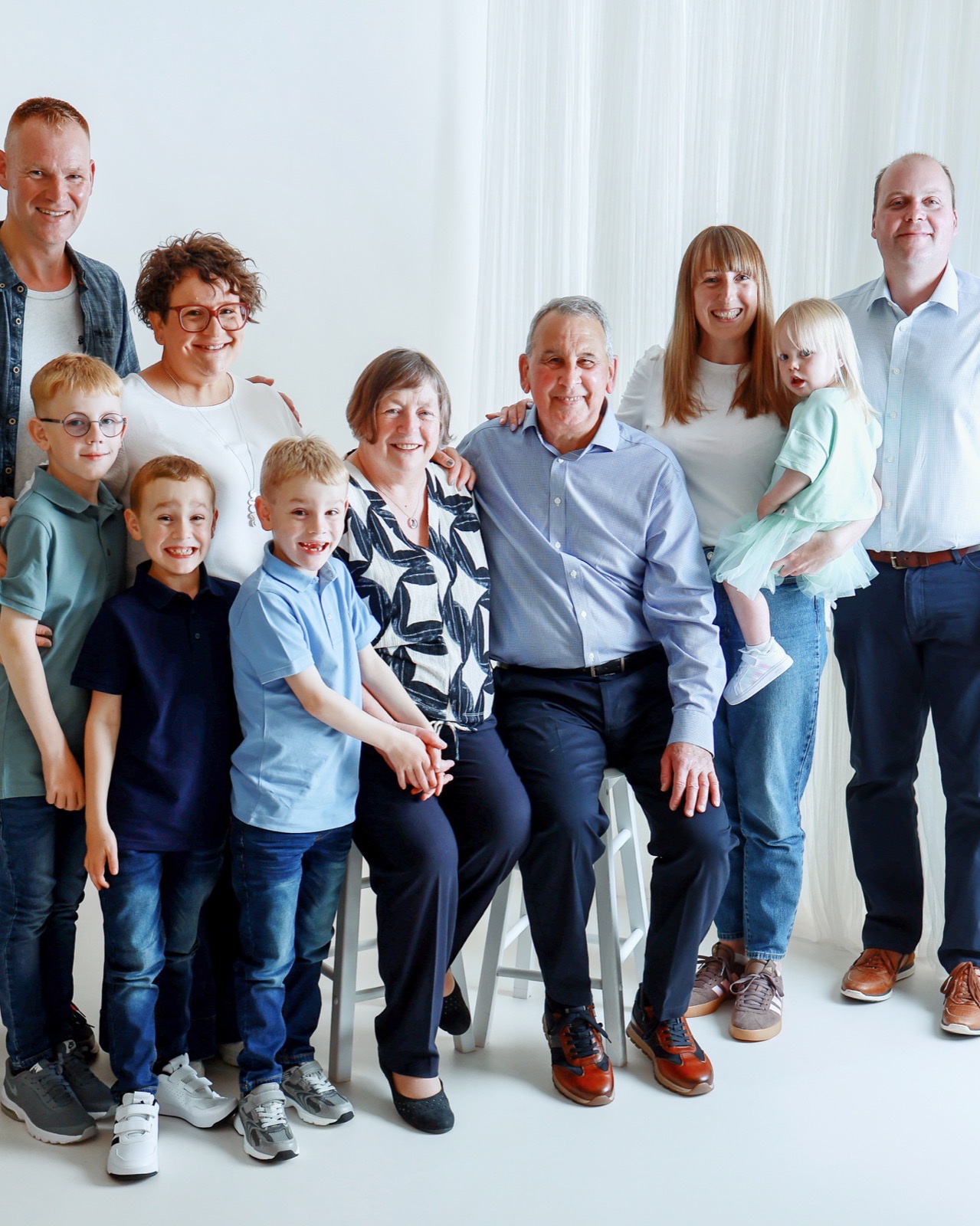 Extended family of ten posing together, grandparents seated centre with adult children, partners and grandchildren around them, one toddler in a mint dress
