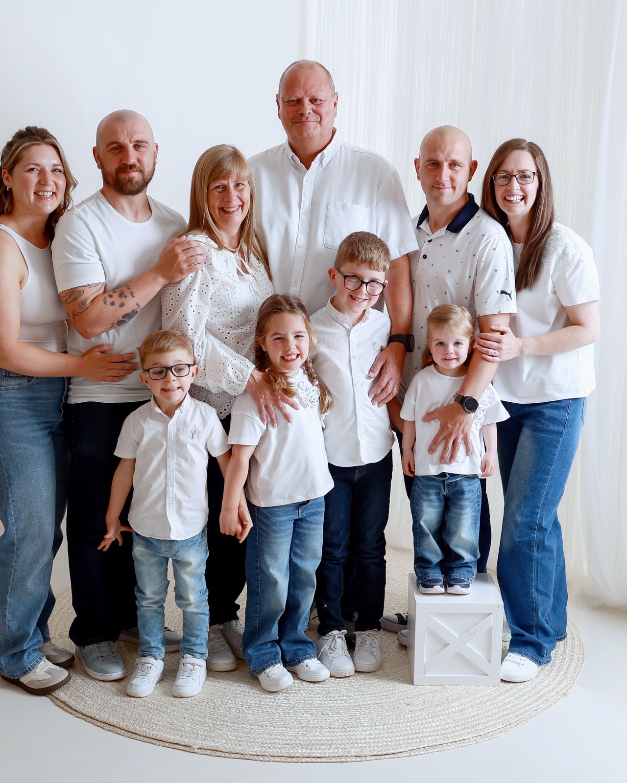 Large extended family of ten in matching white outfits, standing together on a round woven rug