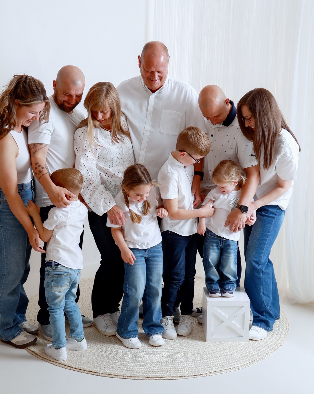 Large extended family in a candid huddle, everyone looking down at the children in the middle