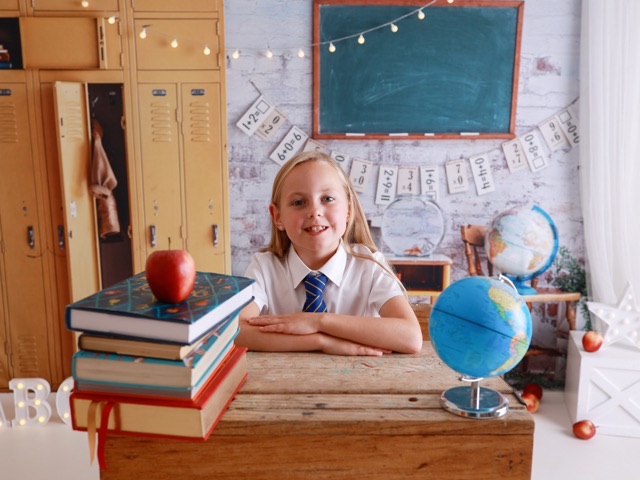 Girl smiling at a school desk with lockers and a globe, from a school photography session