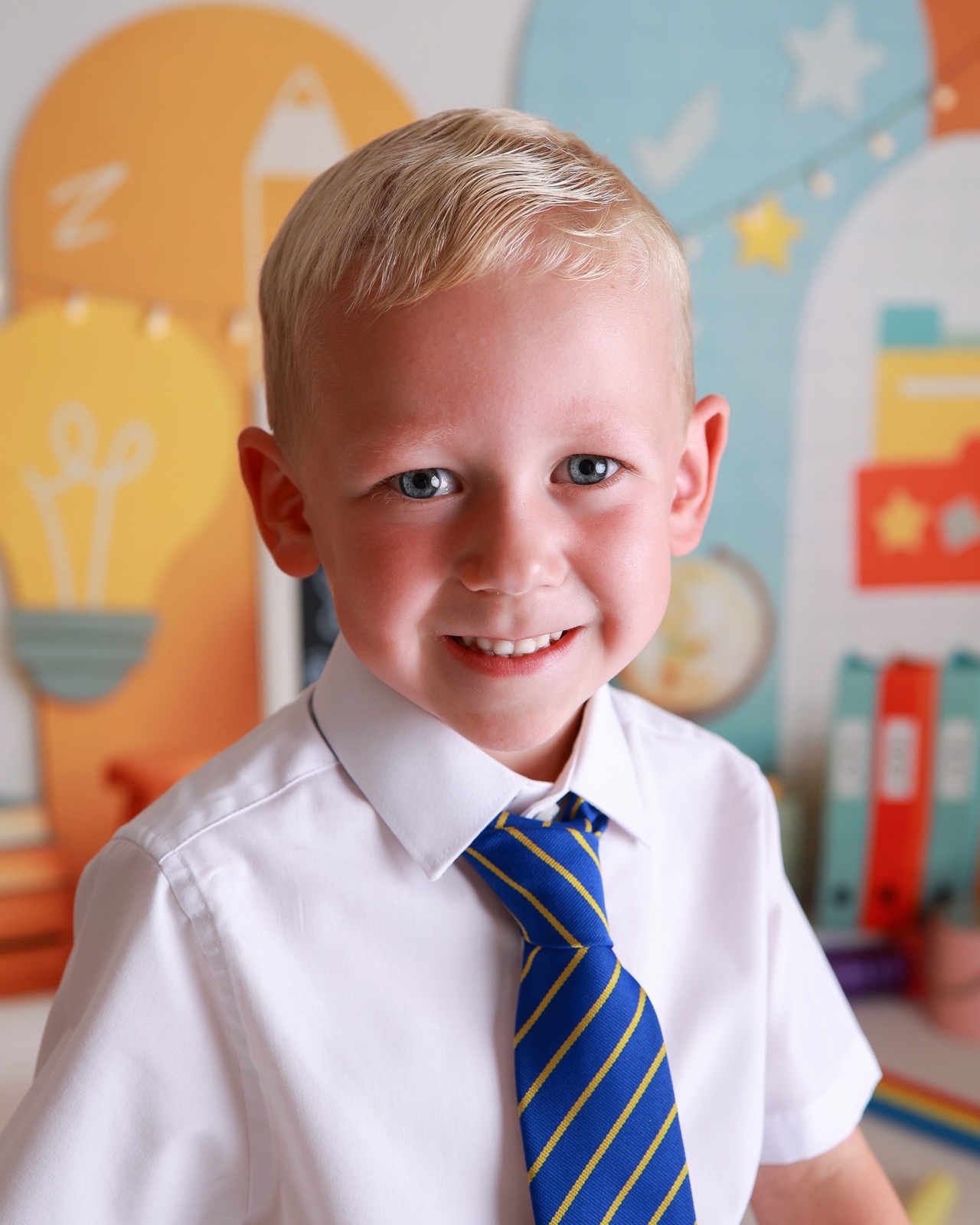 Close-up portrait of a smiling boy in a white shirt and blue striped tie, classroom-themed backdrop