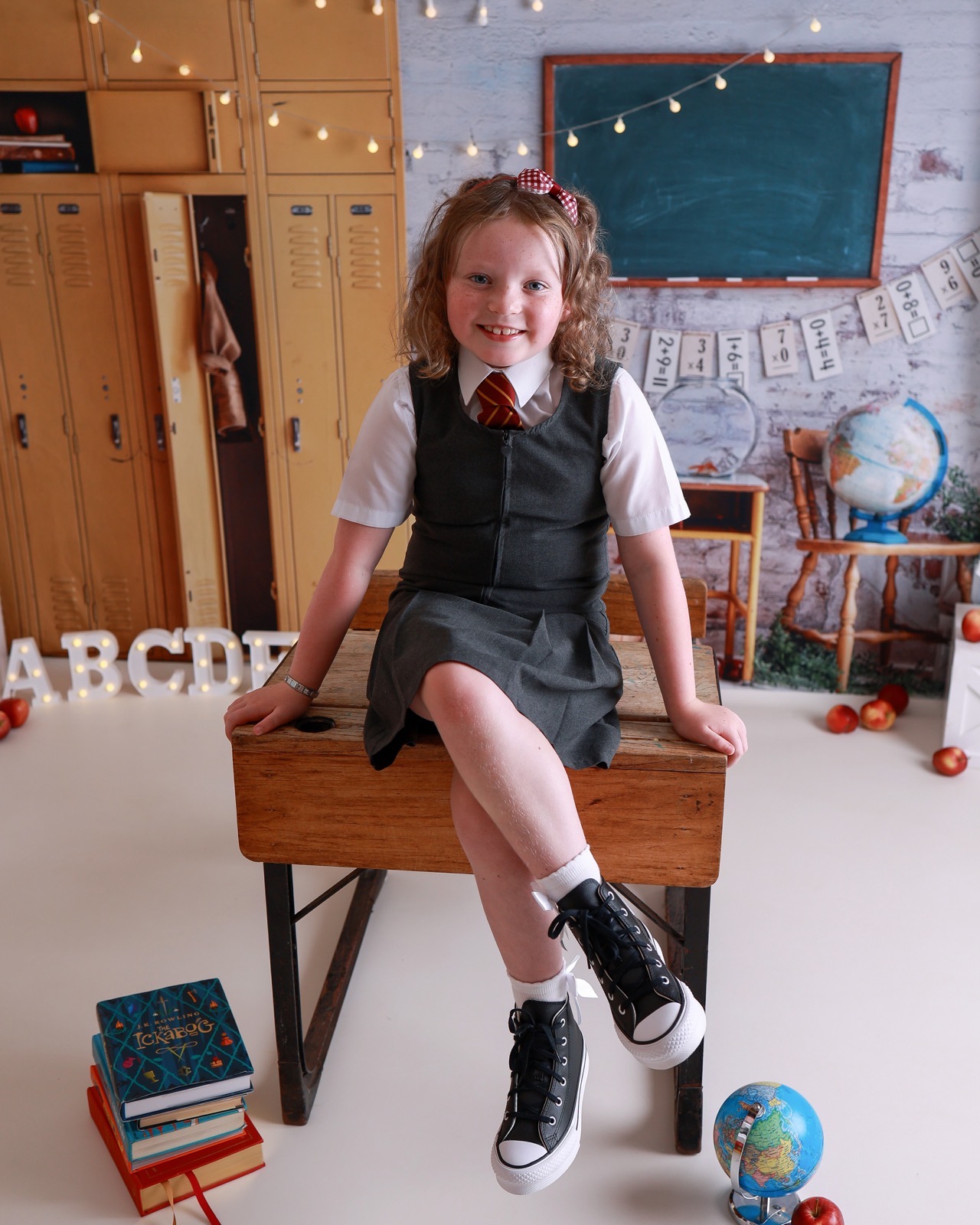 Girl sitting on the edge of a wooden desk with legs crossed, grey pinafore and black lace-up shoes