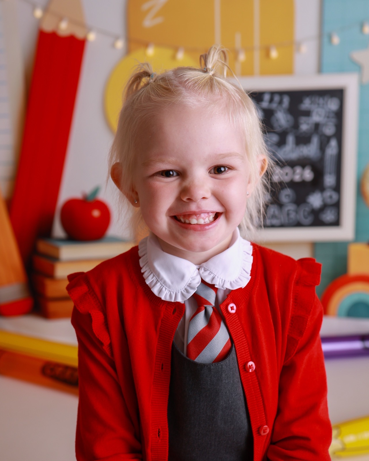 Close-up portrait of a smiling girl with a red hair bow, red cardigan with a ruffled white collar