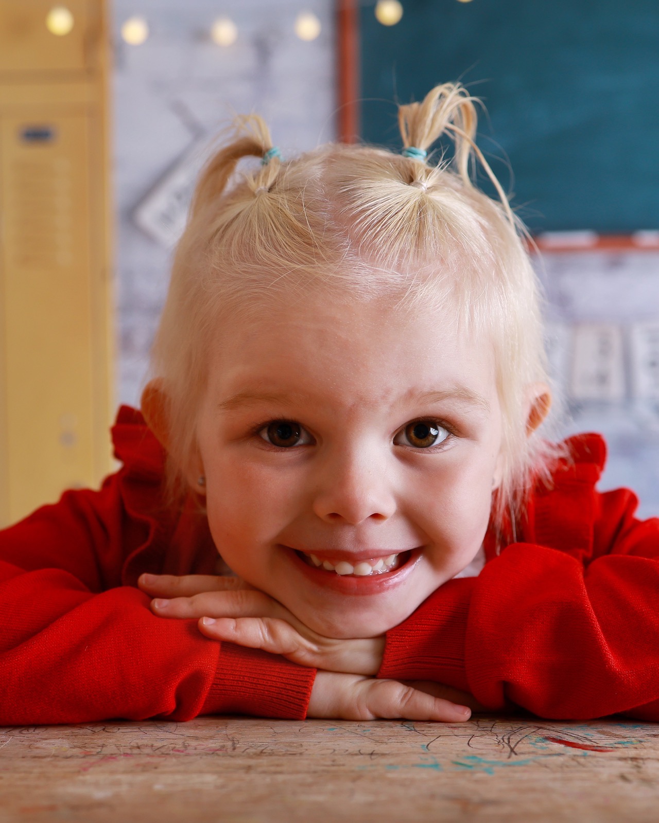 Girl standing by school lockers holding a red book, grey pinafore and striped tie