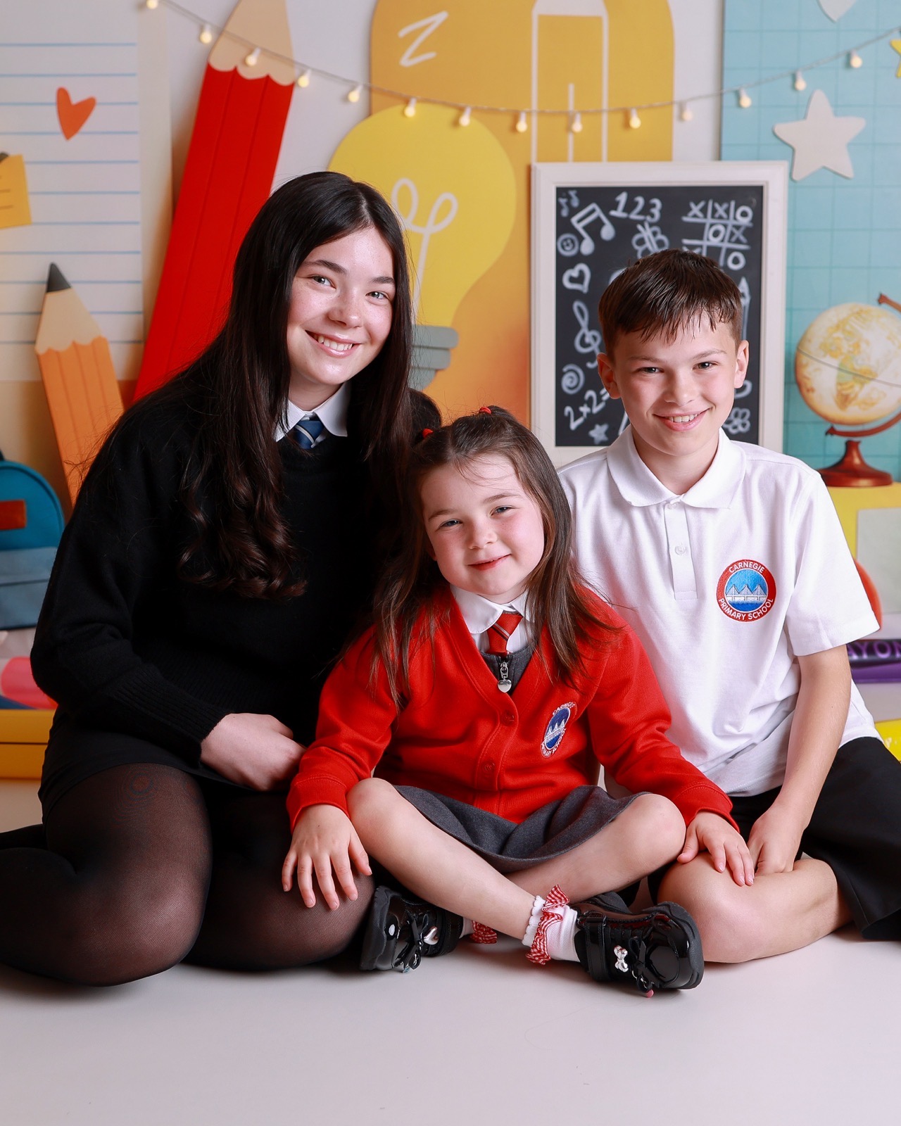 Older sister sitting with her younger sister and brother, mixed school uniforms, all smiling