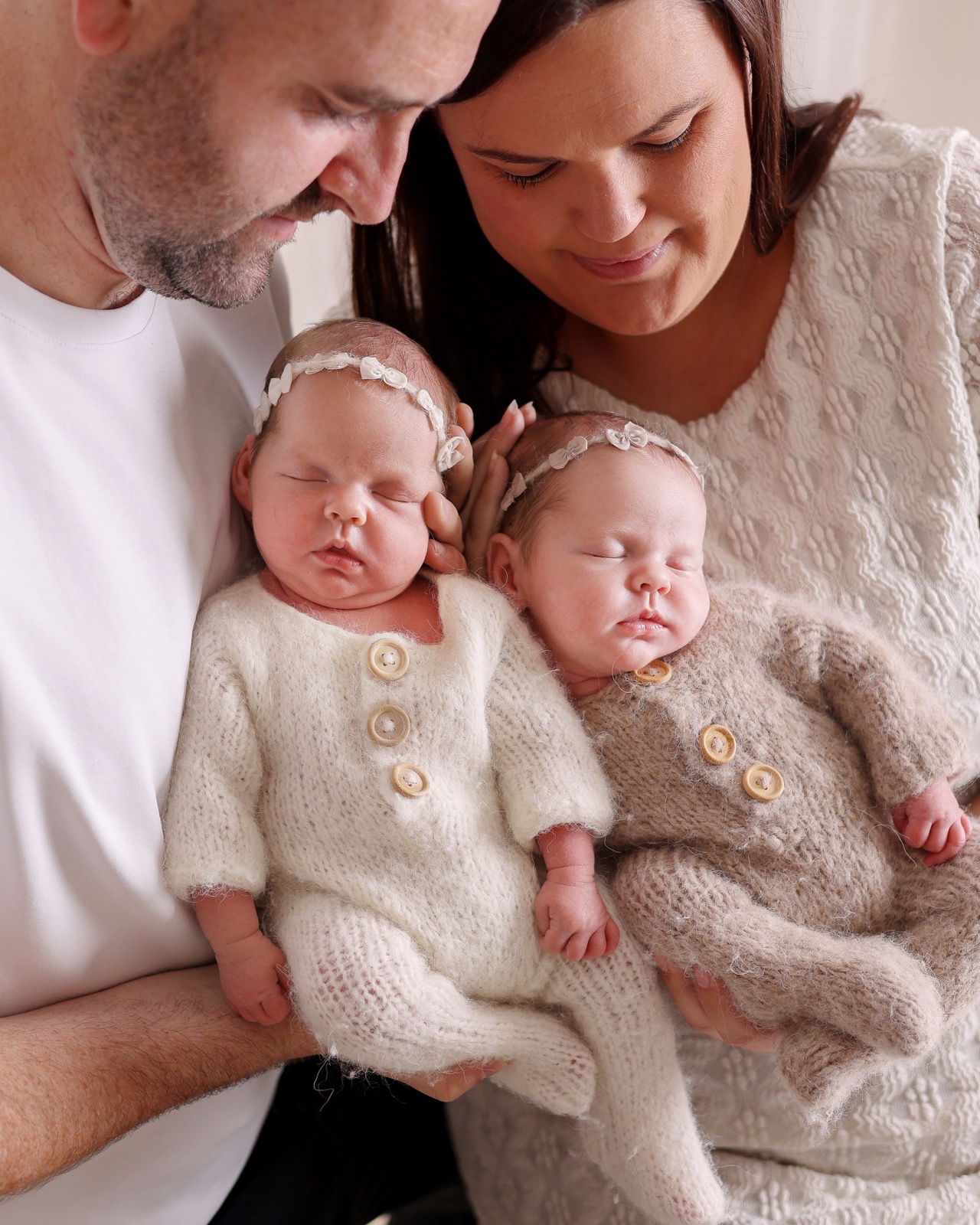 Mum and dad leaning in together over their sleeping newborn twins, each cradling one baby's head