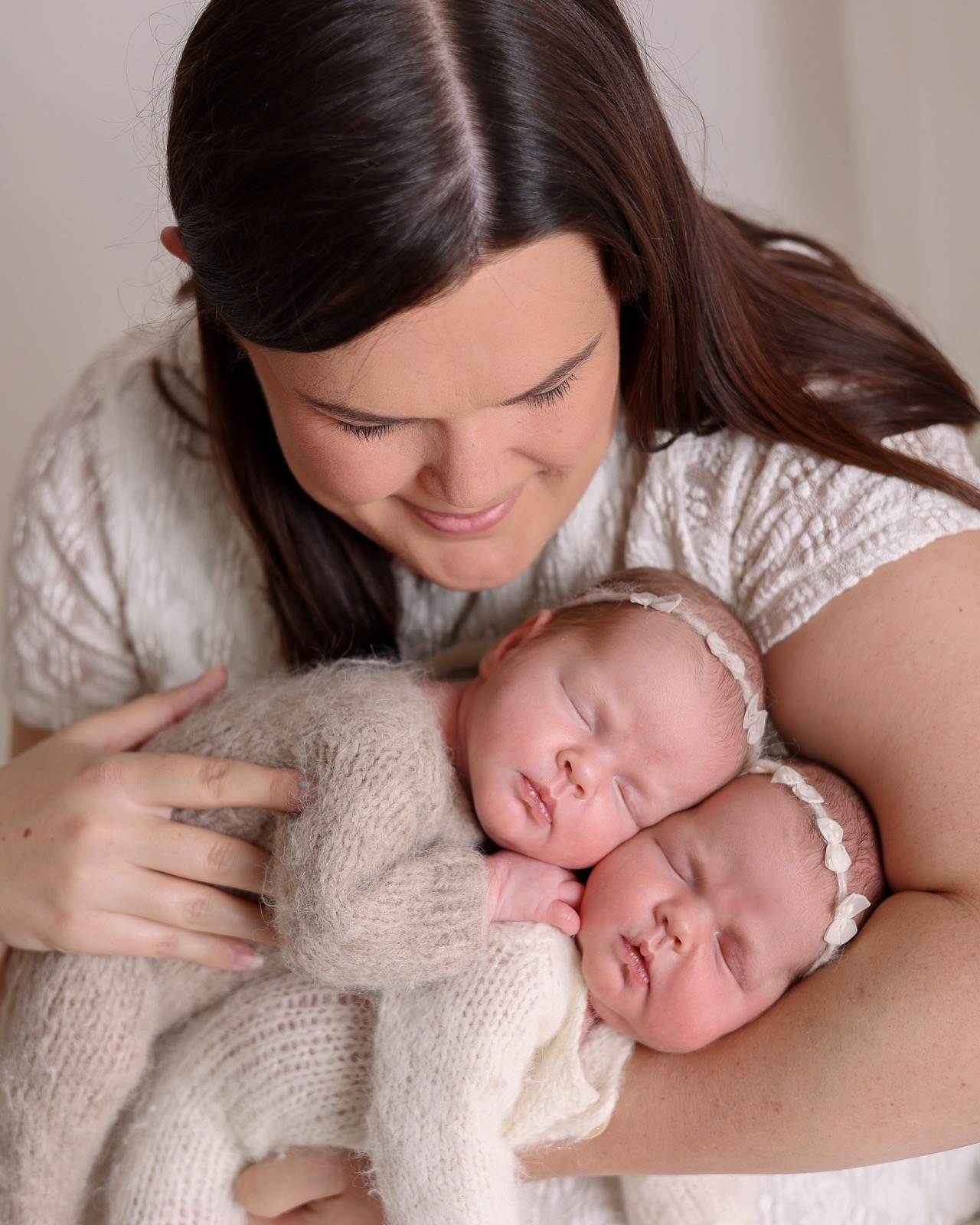 Mum smiling down at her sleeping newborn twins, one resting on each shoulder