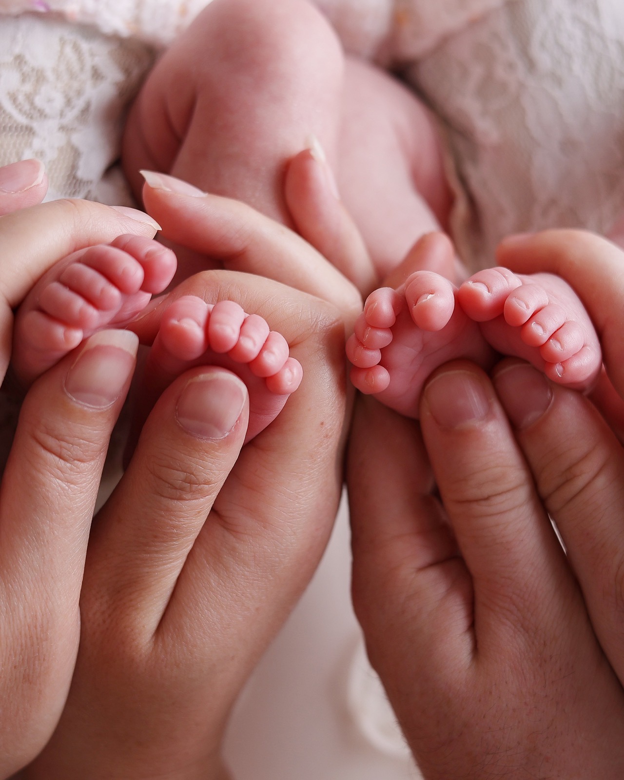 Close-up of newborn twins' tiny feet held together in their parents' cupped hands