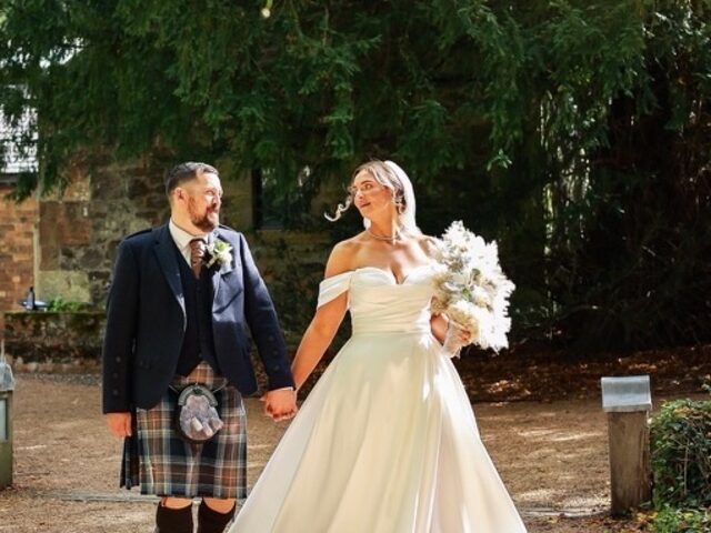 Bride and groom holding hands and smiling at each other, walking beneath a sunlit tree, from a wedding photography session