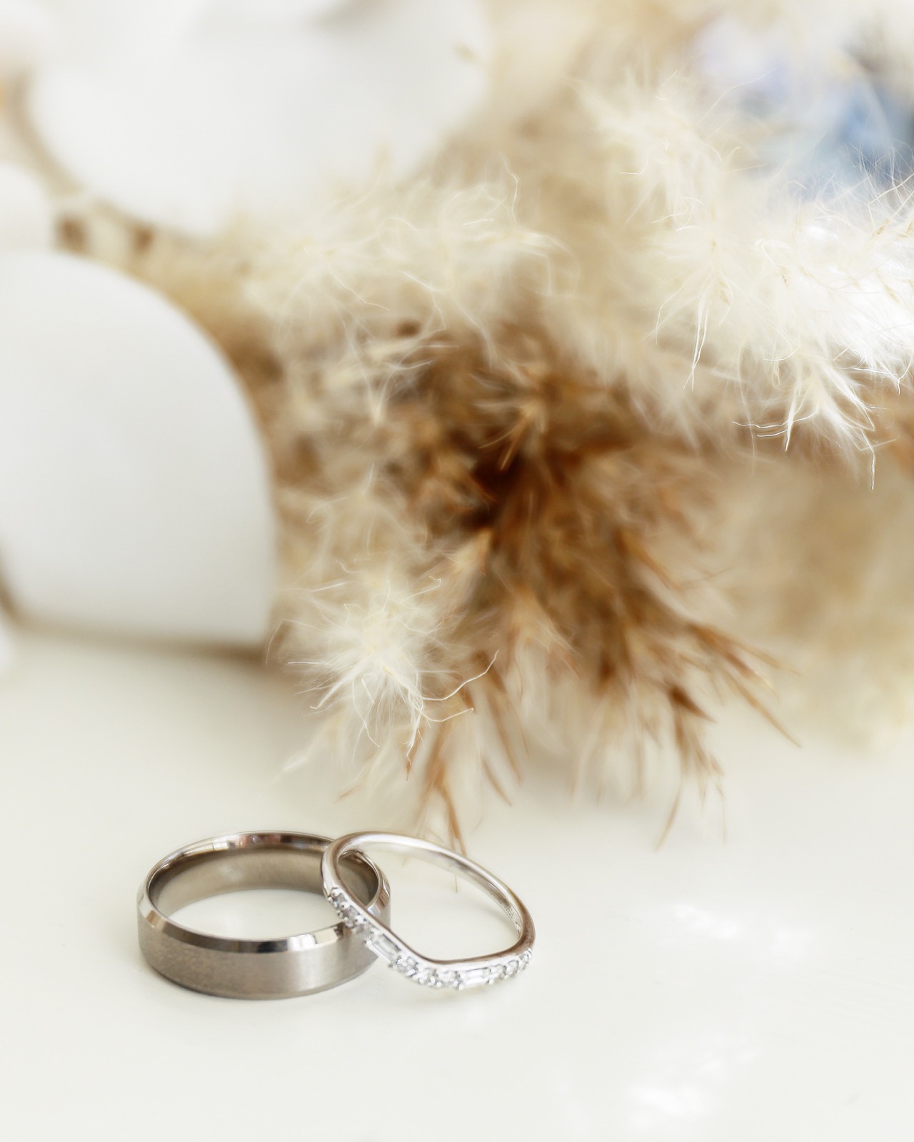Close-up of two wedding rings resting together beside a dried pampas grass bouquet detail