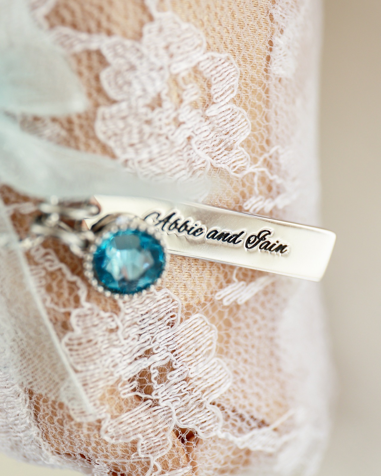 Close-up of a personalised garter charm with a blue crystal detail