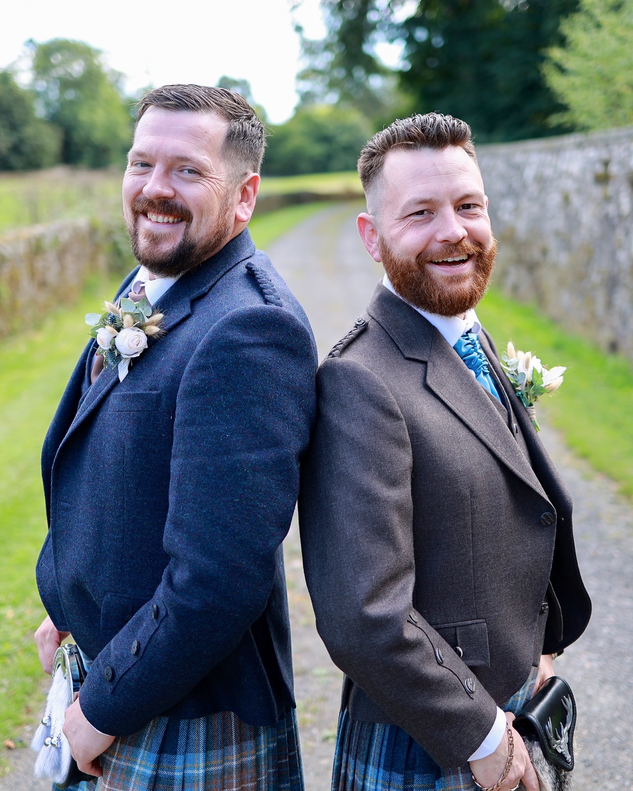 Two groomsmen in tweed jackets and tartan kilts standing back to back, laughing