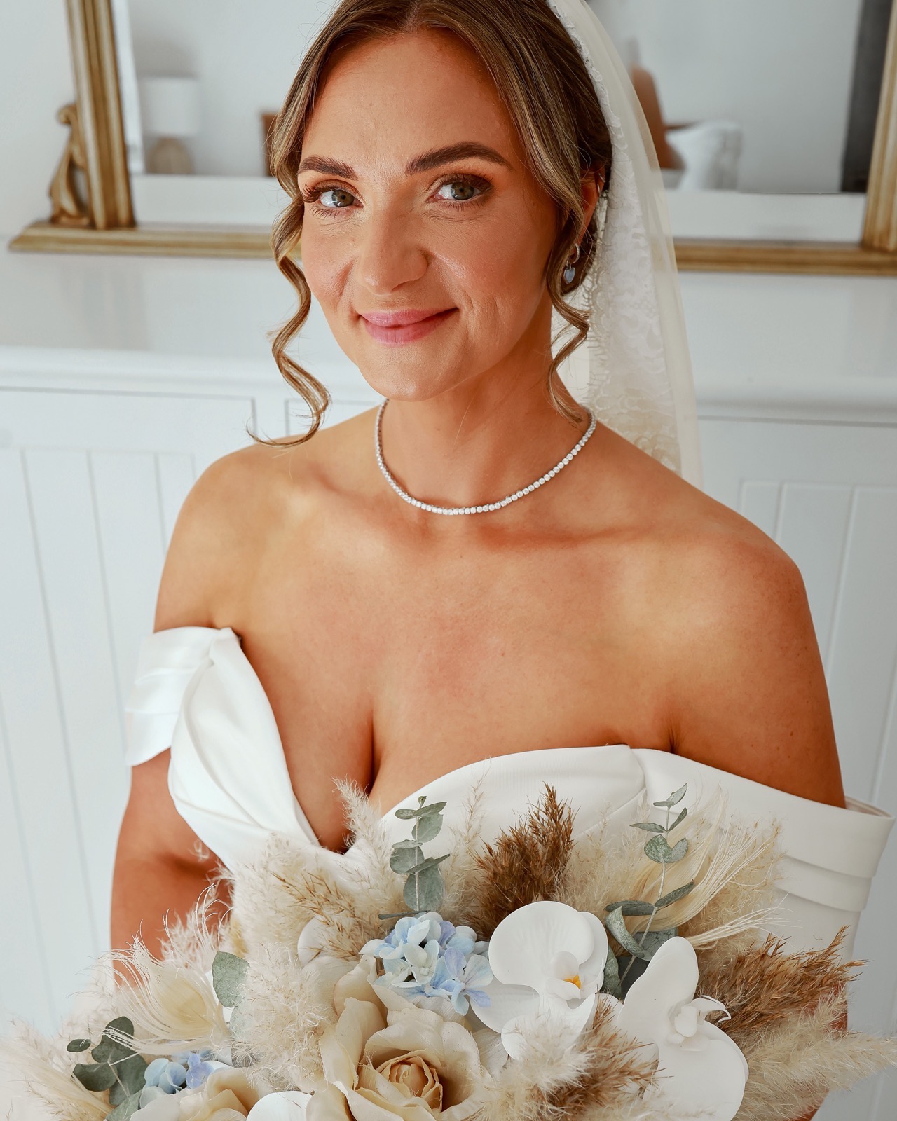 Close-up portrait of a smiling bride in a pearl necklace and veil, holding her bouquet