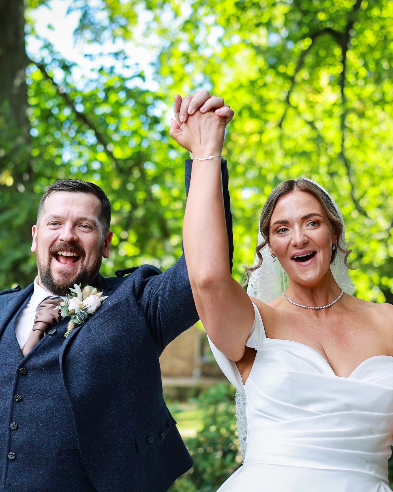 Close-up of the bride and groom raising their joined hands triumphantly, both laughing