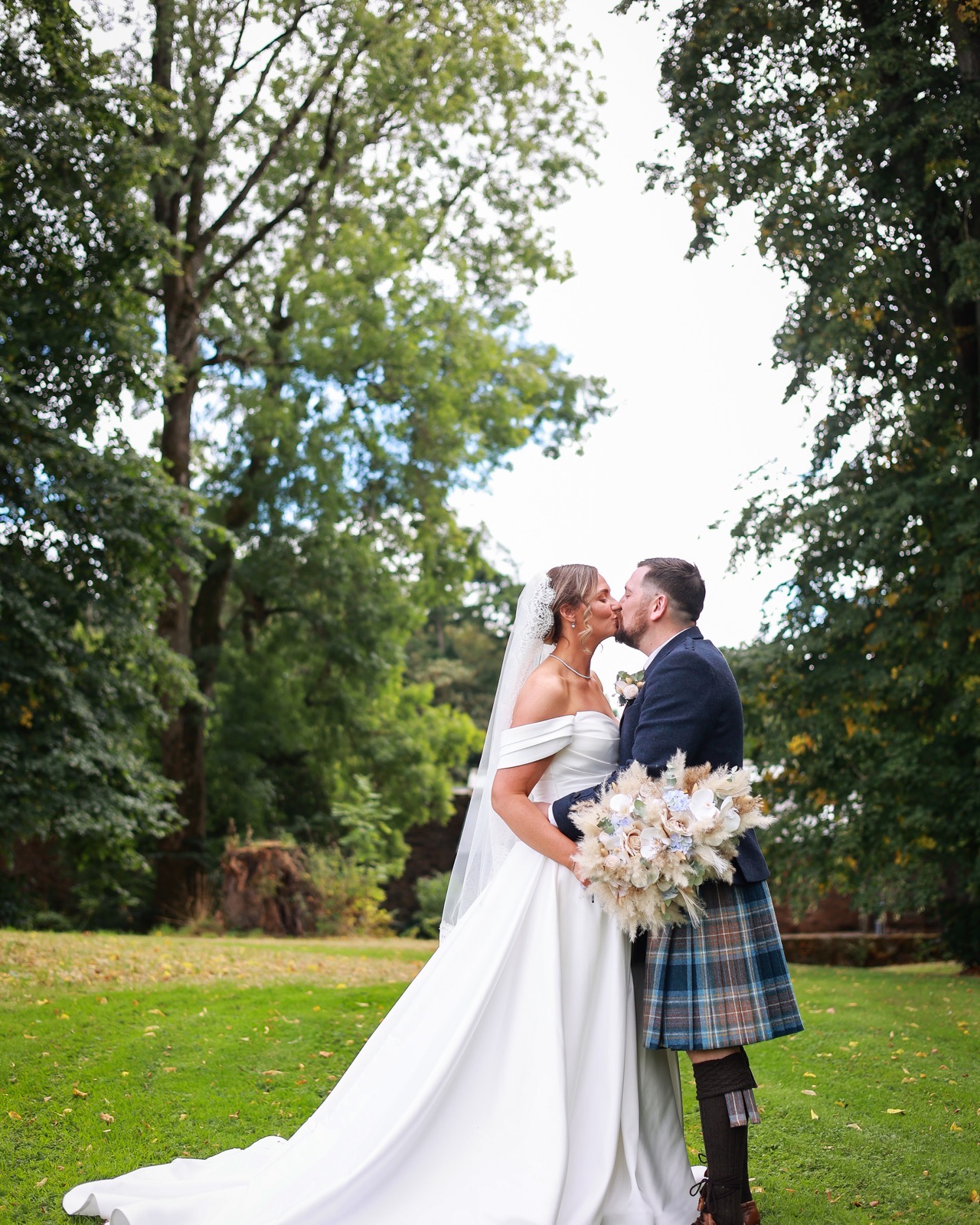 Bride and groom kissing on the lawn, groom in a kilt