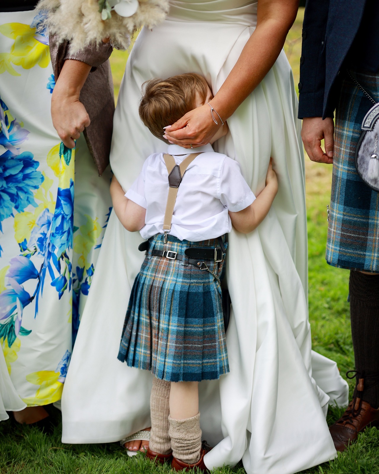 Young boy in a tartan kilt outfit hugging the bride from behind