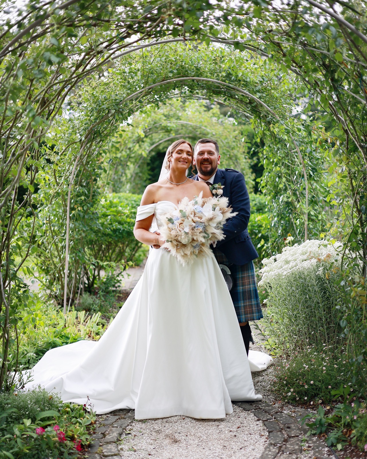 Bride and groom smiling together under a rose-covered archway tunnel