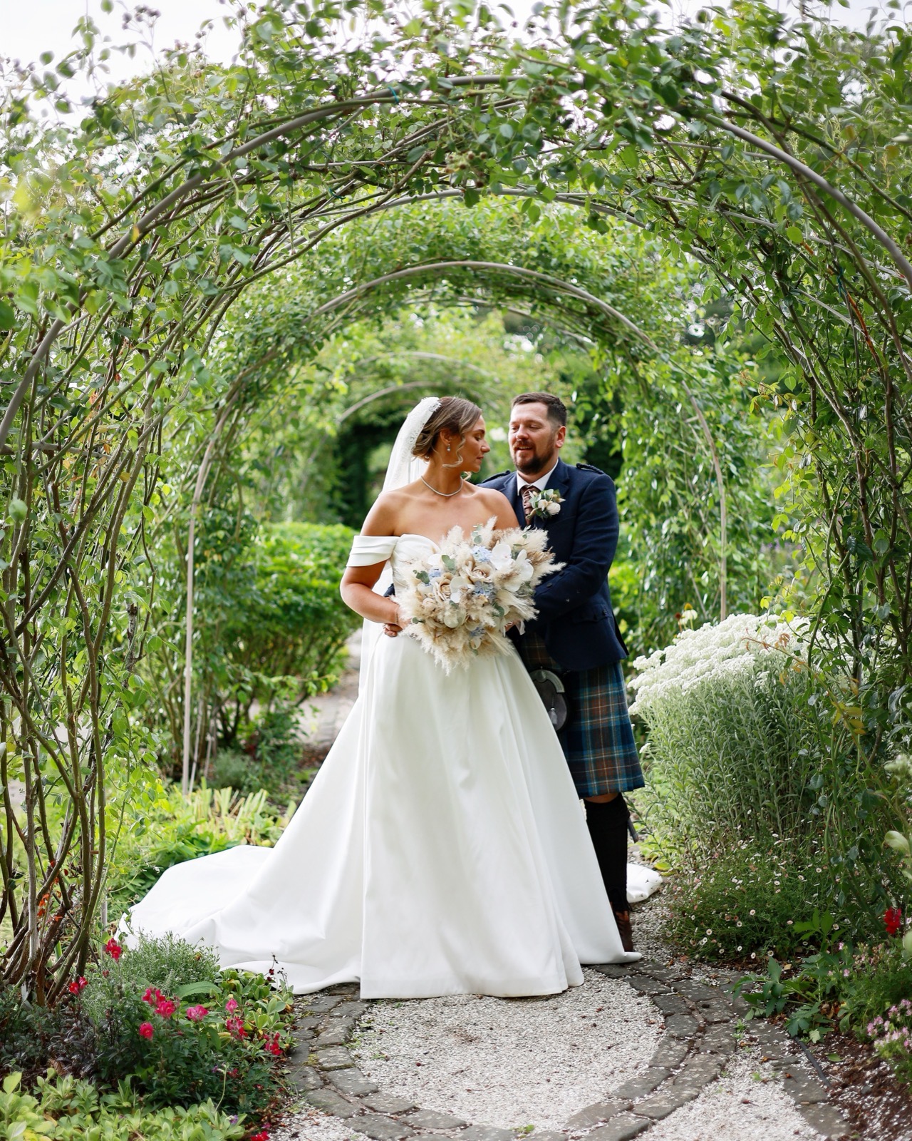 Bride and groom gazing at each other under a rose-covered archway tunnel