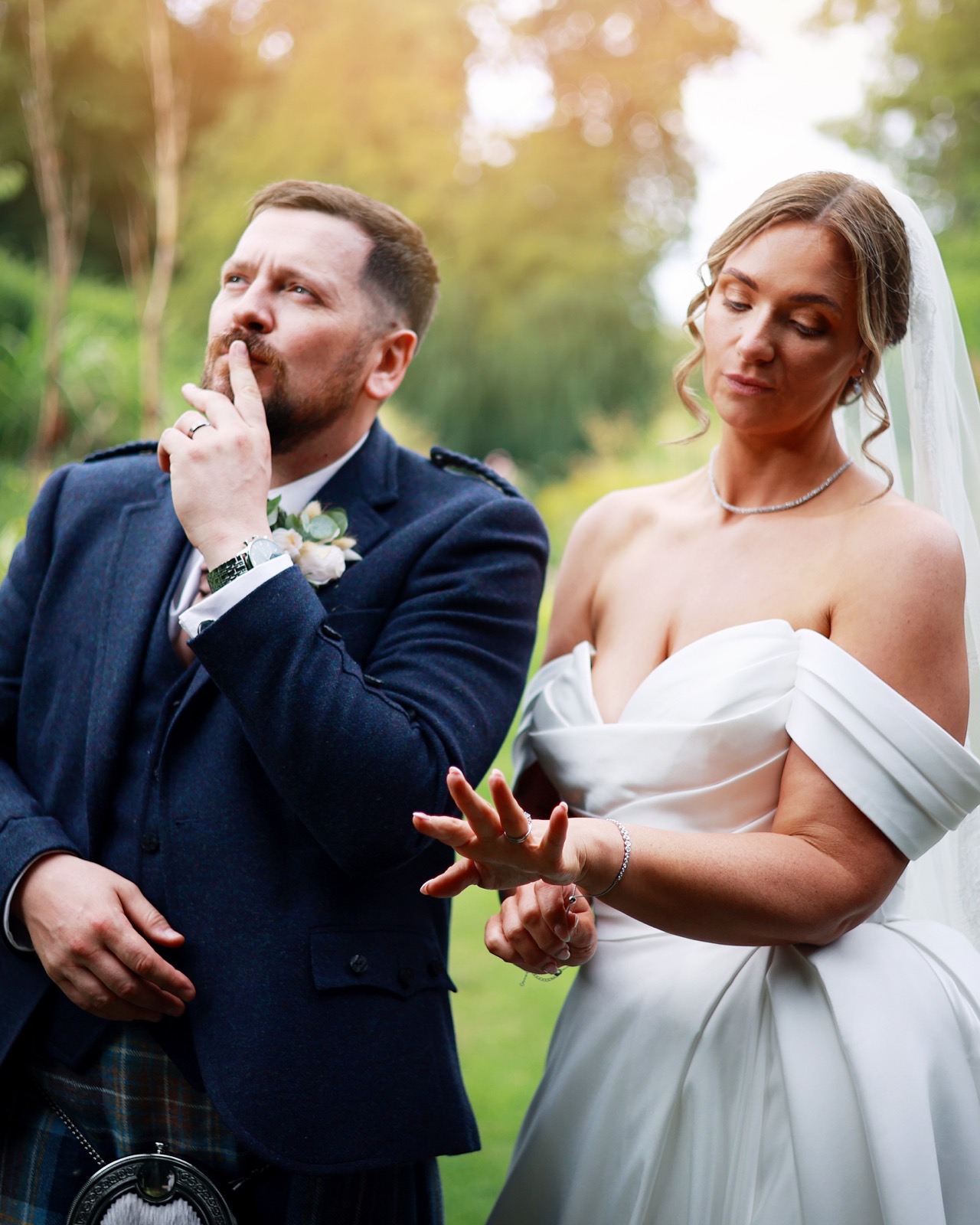 Groom in a playful thinking pose beside the bride, who looks at her nails